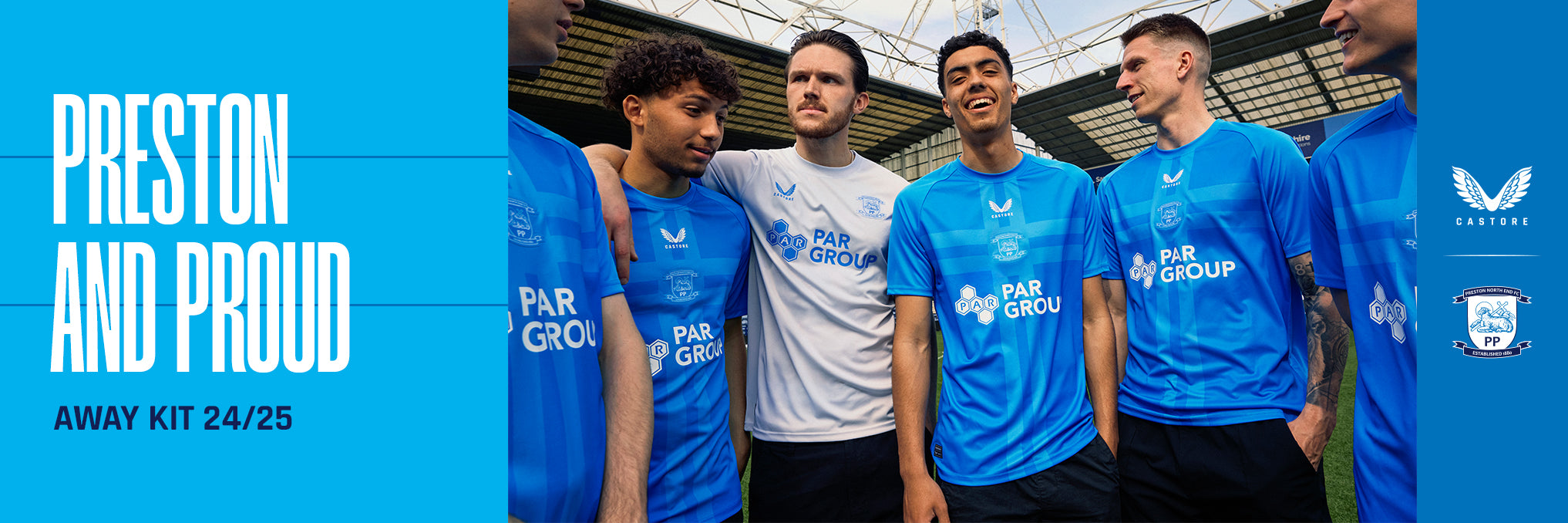 Group of players in blue away kits posing together on a football pitch with blue banners on the side.
