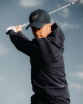 Male golfer in midnight navy performance hoodie mid swing against a cloudy sky