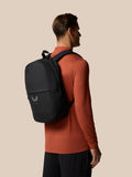 Back view of a man wearing a gunmetal Castore Core Backpack over an orange top.