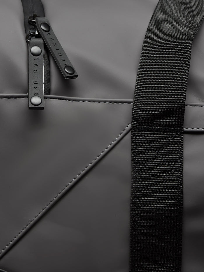 Detail of Core Holdall zipper pull on a black PU bag with a textured strap