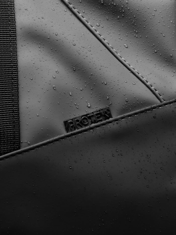 Close up of Core Holdall exterior in gunmetal black with water droplets on the PU surface and a padded strap