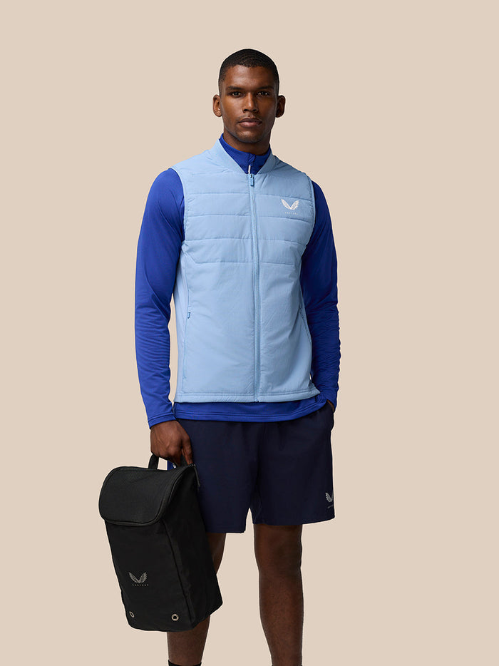 Male model wearing a light blue puffer vest holds the black Active Boot Bag.