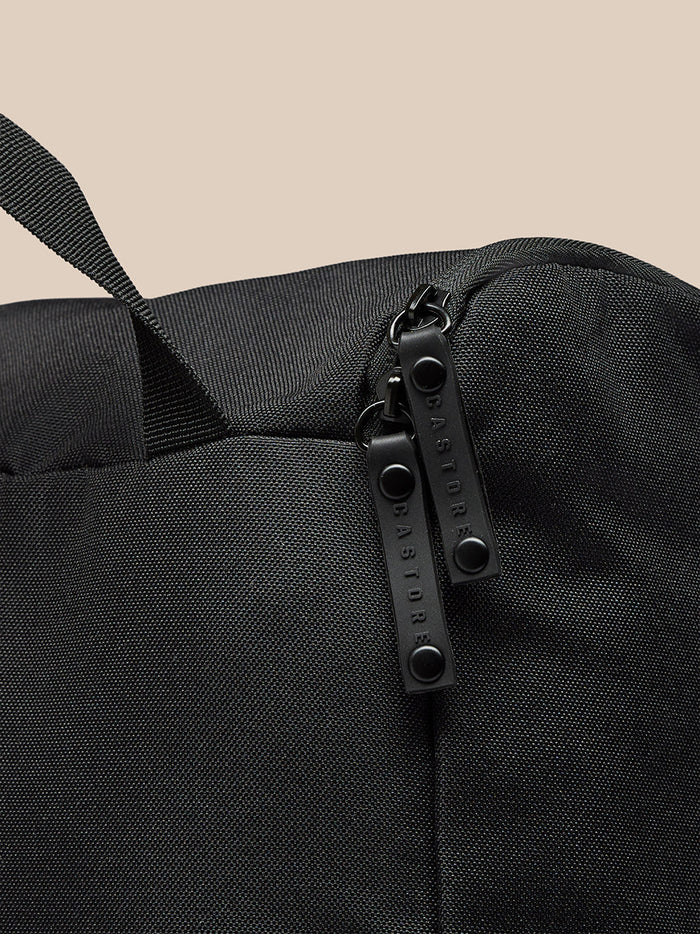 Close-up of black Castore boot bag fabric showing a top strap and dual zipper pulls.