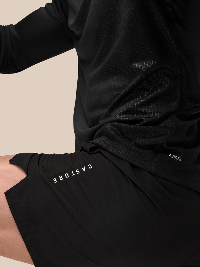 Close-up of black Adapt Training 6-inch shorts showing Castore branding along the left thigh and Aertek logo at the rear.