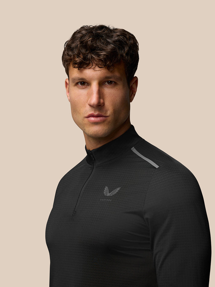 Front view of a man wearing black Apex Training Quarter Zip Top with stand collar and reflective Castore branding on the chest.