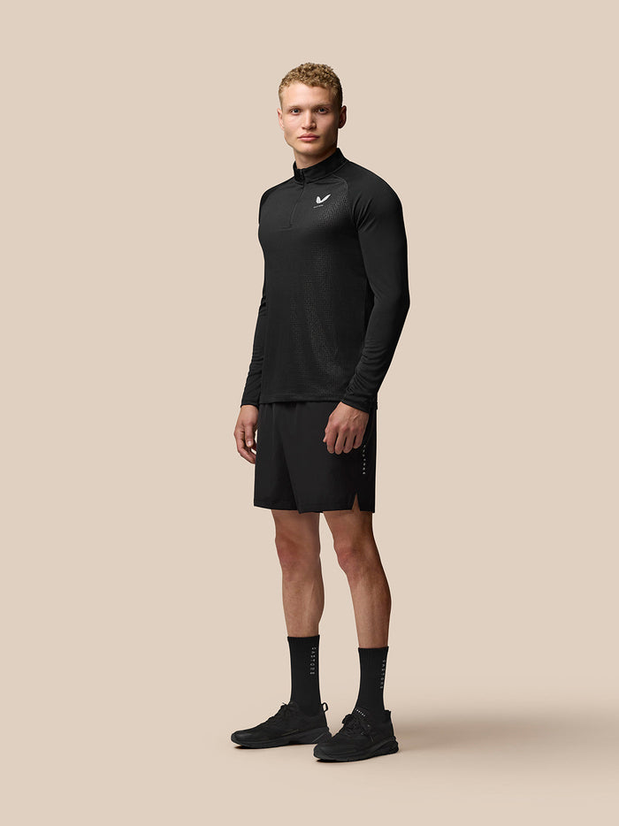 Full-body shot of man in black Adapt Print Quarter Zip Top with long sleeves and geometric pattern paired with black shorts.