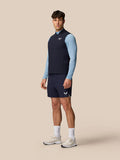 Model wearing navy Apex Training Gilet over a light blue long sleeve top and navy shorts with Castore logo on the chest