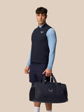 Male model wearing navy Apex Training Gilet over a light blue top with a gym bag