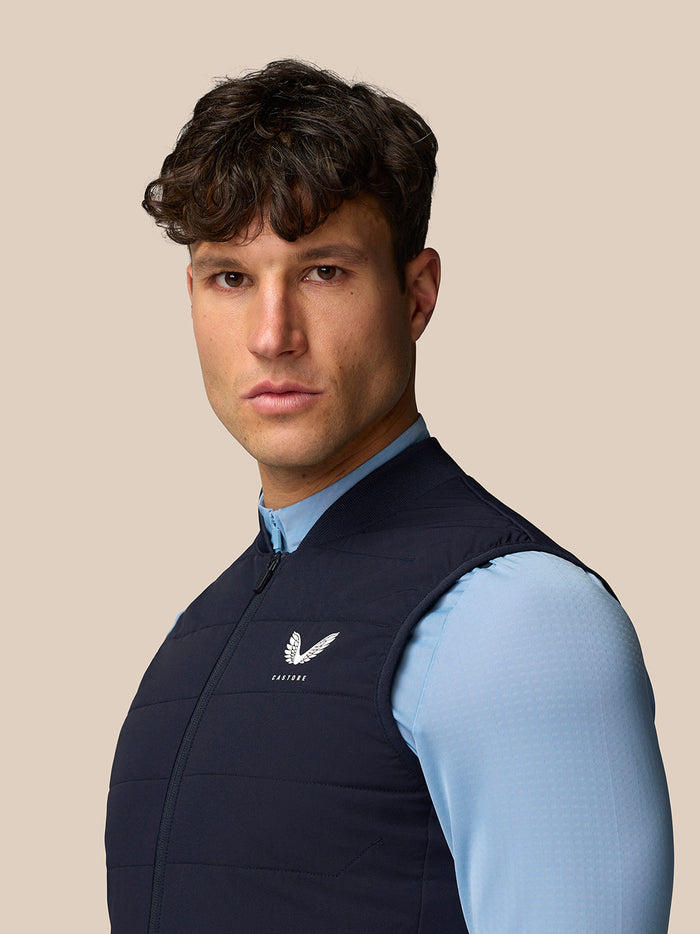 Three-quarter view of male model wearing navy Apex Training Gilet; chest Castore logo and front zip visible.