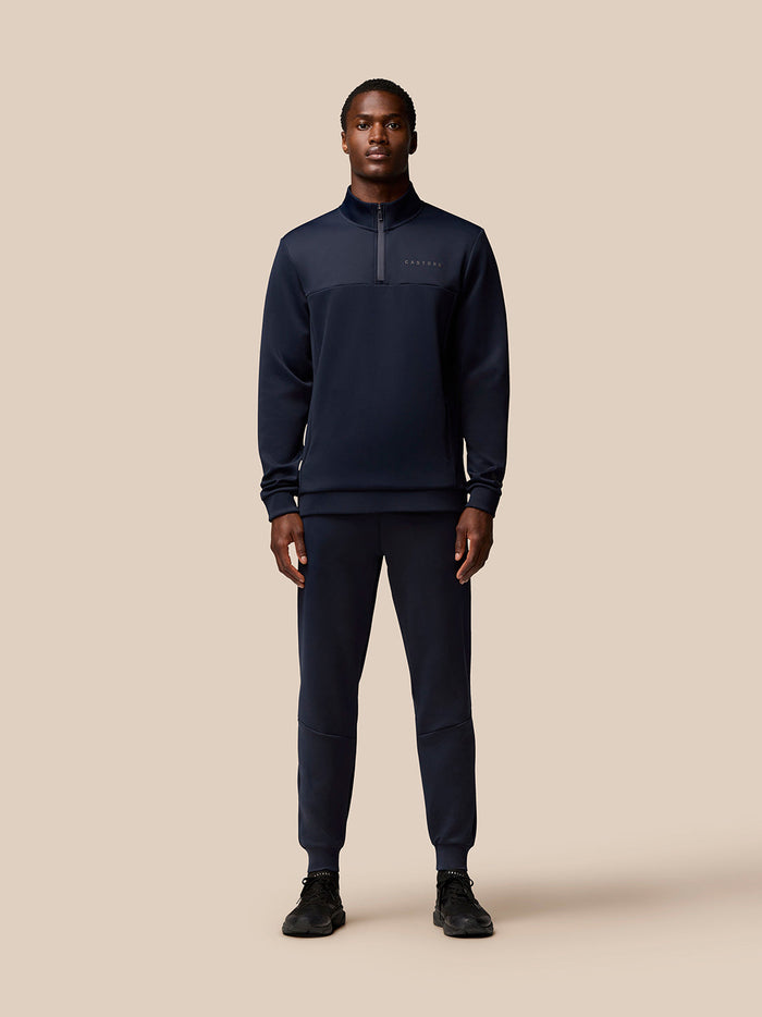 Full body shot of a man wearing navy Flex Lifestyle Joggers with a zip neck top on a beige background
