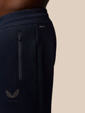 Close-up of navy joggers waist with Protek branding, a vertical side zip pocket, and the Castore emblem at the hip.