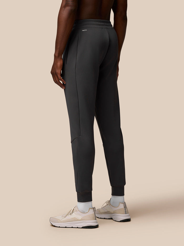 Back view of a man wearing charcoal Flex Joggers with elastic cuffs and left hip Protek branding.