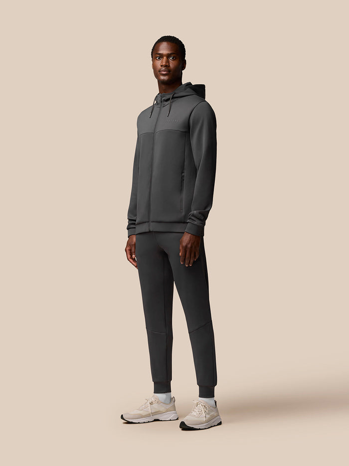 Full-body shot of a man in charcoal Flex Joggers paired with a matching zip hoodie.