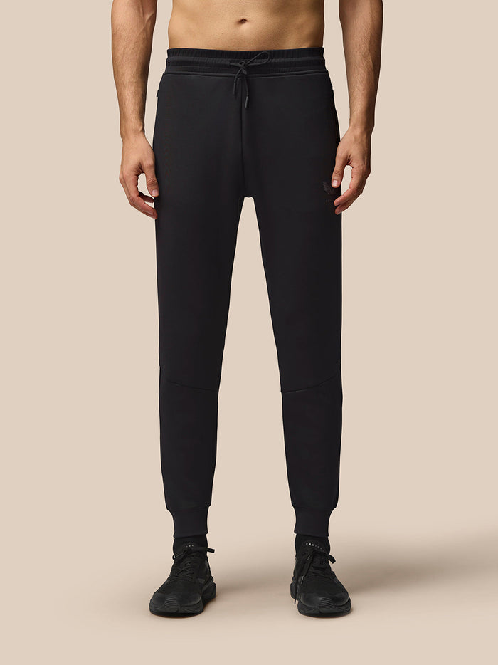 Front view of a man wearing black Flex Joggers with an external drawcord, rib cuffs, and Castore branding at the left thigh
