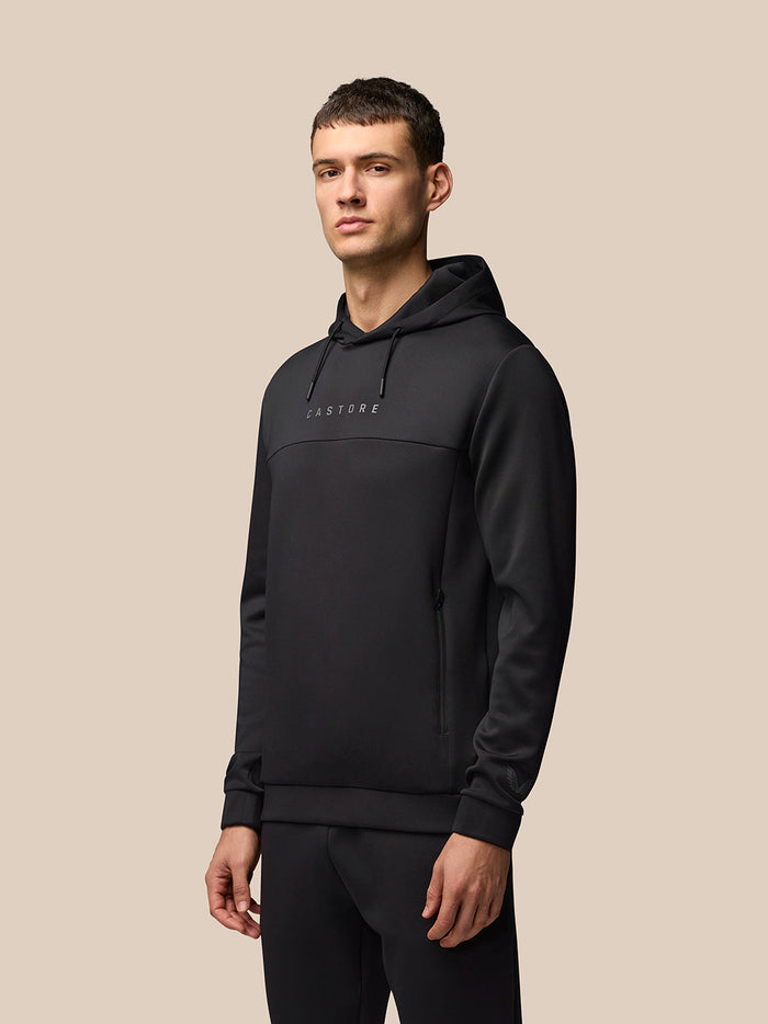 Male model wearing black Castore Flex Long Sleeve Hoodie with ProTek water resistance and a centered Castore logo on the chest