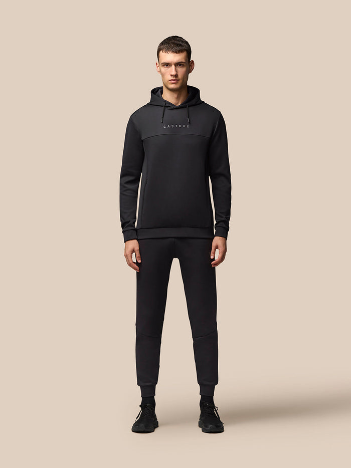 Full body shot of male model in black Castore hooded top with chest logo and matching joggers