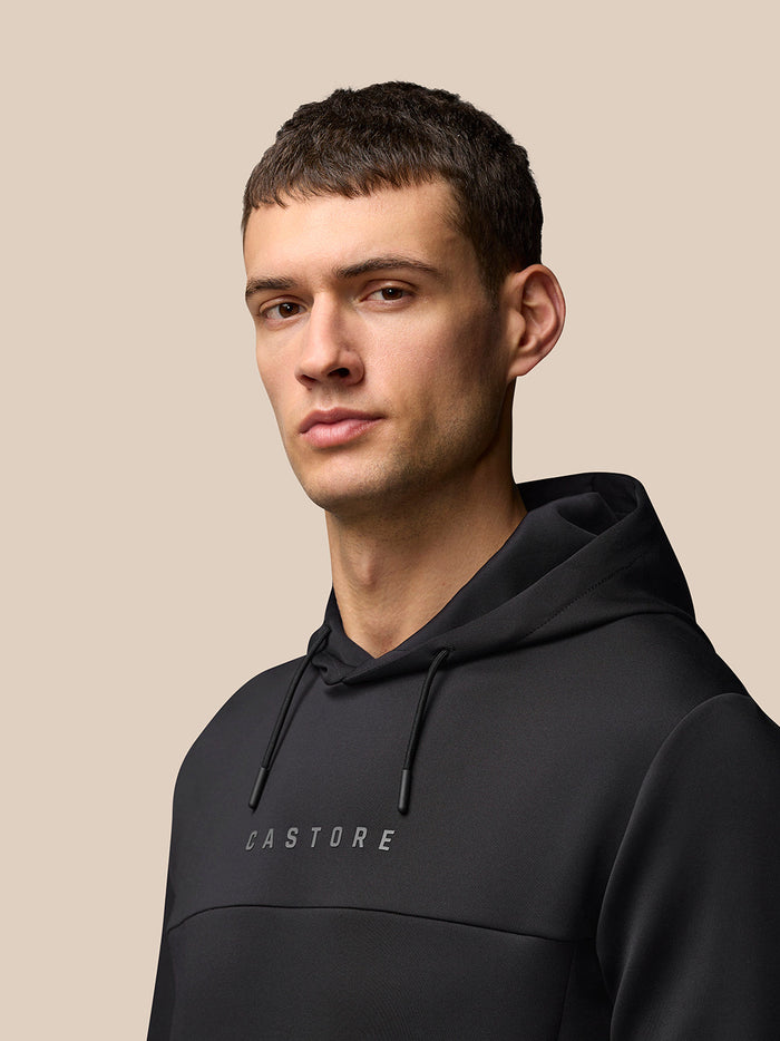 Male model wearing black Castore Flex Long Sleeve Hoodie with hood and center chest Castore logo