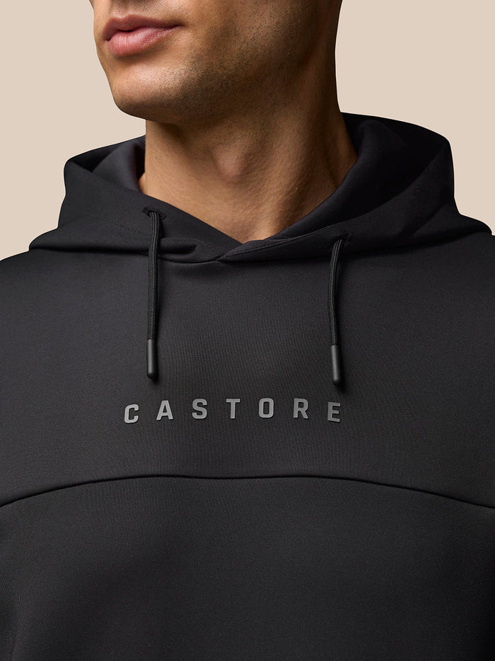 Close up of the black Castore Flex Long Sleeve Hoodie highlighting the central Castore logo on the chest and hood drawstrings
