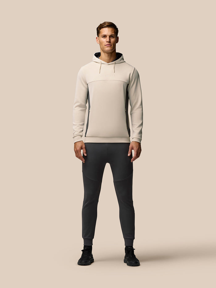 Beige hoodie sleeve close-up showing embossed Castore wing logo and a side zip pocket.