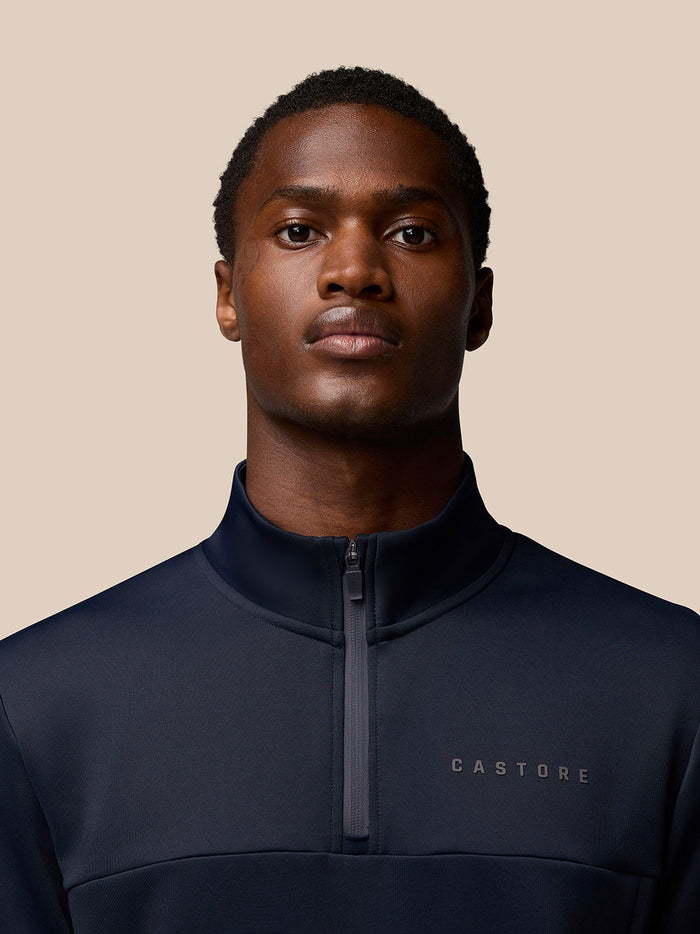 Close-up of a man wearing a navy Castore Flex Lifestyle Quarter Zip with center zipper and left chest branding