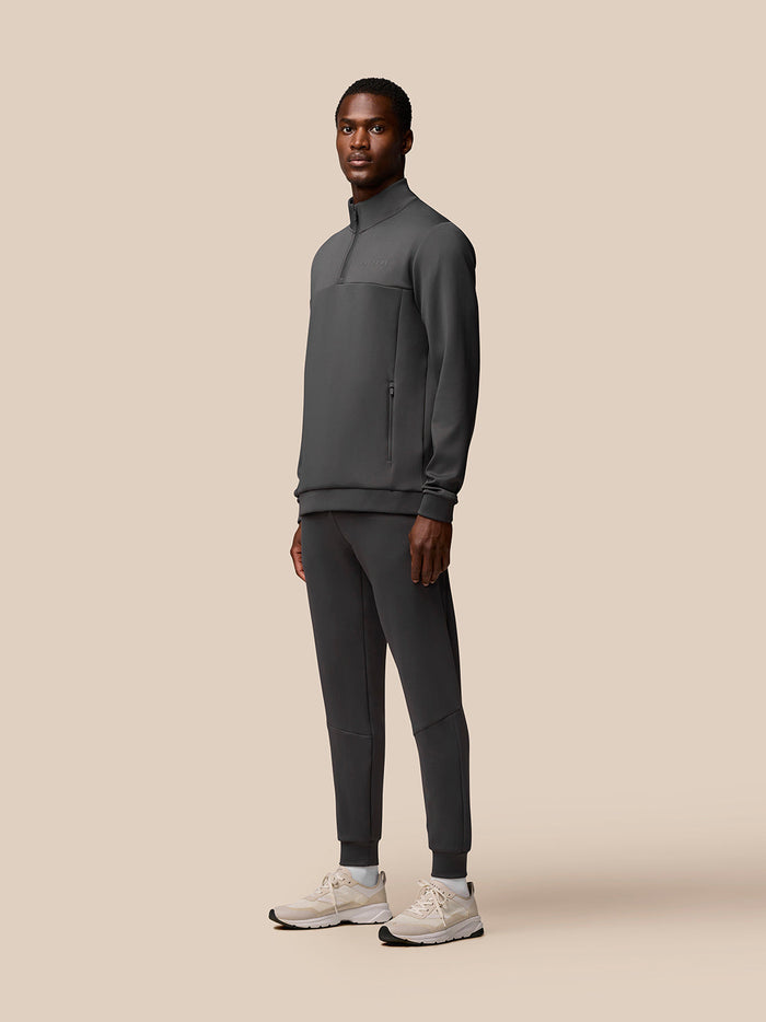 Full body view of a man in charcoal Flex Quarter Zip Top with matching athletic pants and light sneakers.