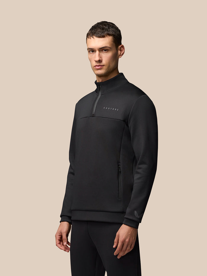 Male model wearing black Flex Lifestyle 1/4 Zip top with zip collar and Castore branding on left chest sleeve and hem