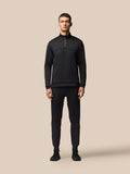 Full-body shot of male model in black Flex Lifestyle 1/4 Zip top with matching joggers against a beige backdrop.