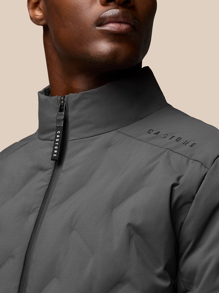 Close-up of Quilts Lifestyle Jacket charcoal highlighting stand collar, front zip and Castore branding.