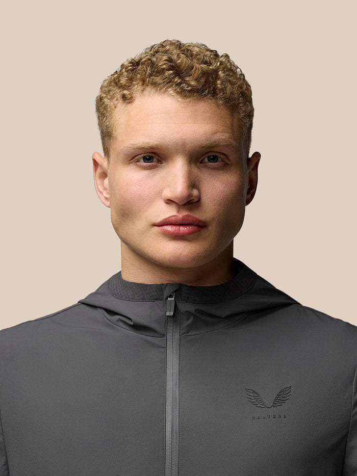 Close up of male model wearing charcoal Lightweight Flex Jacket with zip front and left chest logo.