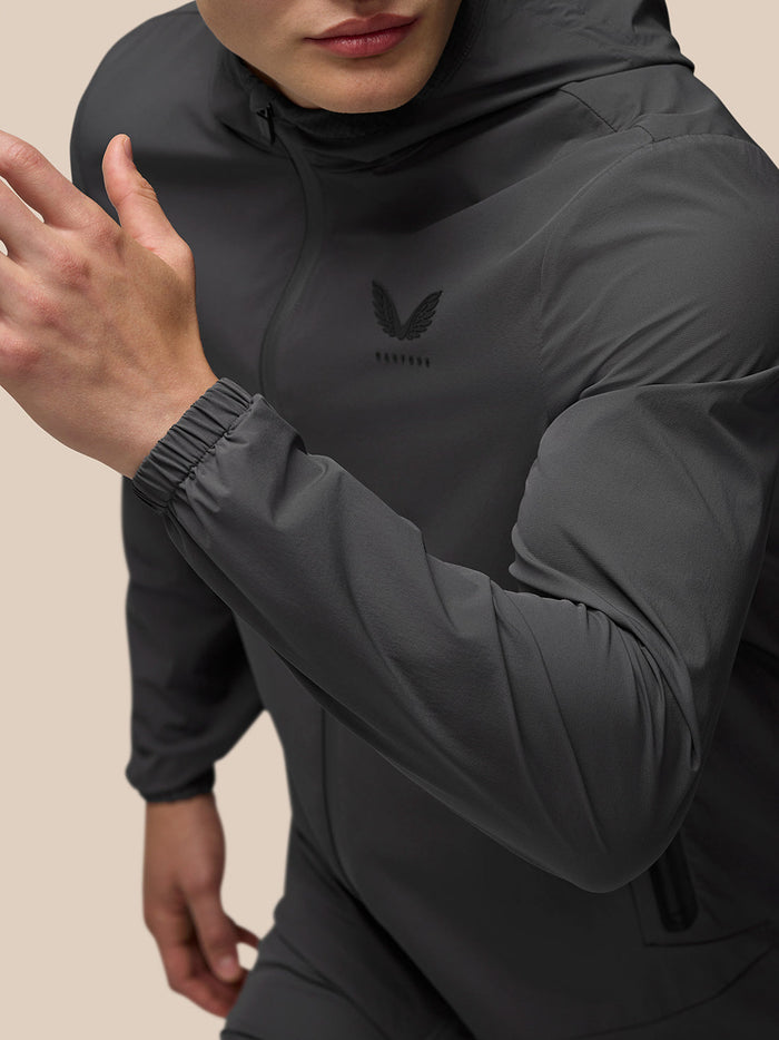 Close-up of upper torso in charcoal Lightweight Flex Jacket showing left chest logo zip pocket and elastic cuff.