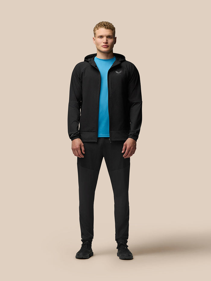 Full-body front view of a model in a black hooded Flex Winterised Jacket zipped over a blue tee, chest logo visible.