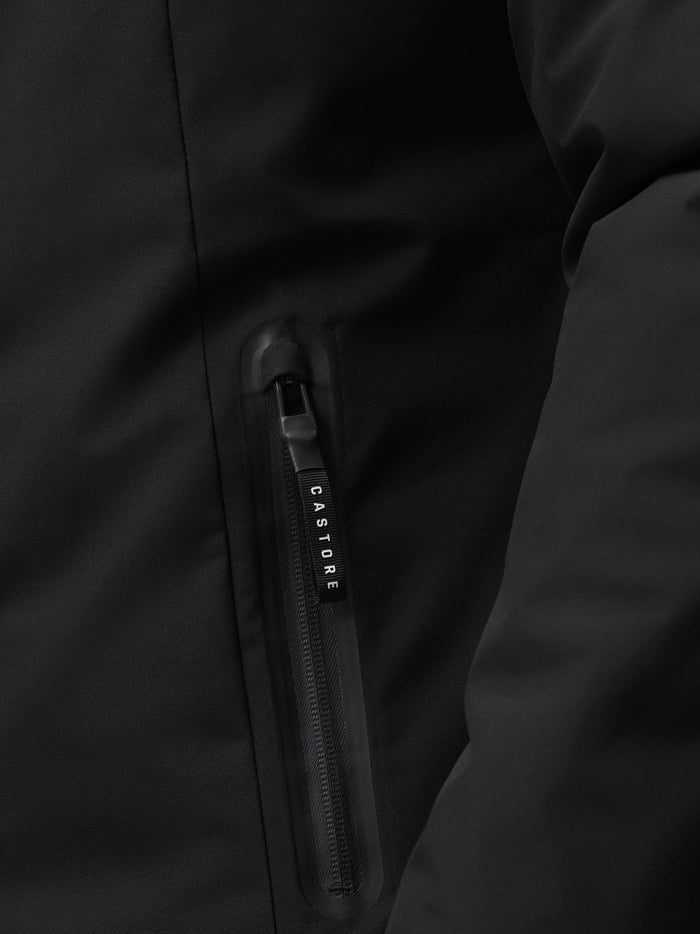 Close-up of black longline jacket fabric with a vertical zip pocket and Castore branding on the zipper.