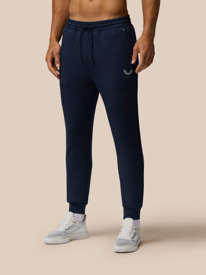 Male model in navy Travel Lifestyle Joggers with elastic drawstring waist and concealed zip pockets, Castore graphic on front.