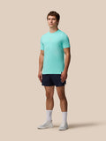 Full-body shot of a man wearing a light aqua Zone Training T-Shirt with navy shorts on a beige background