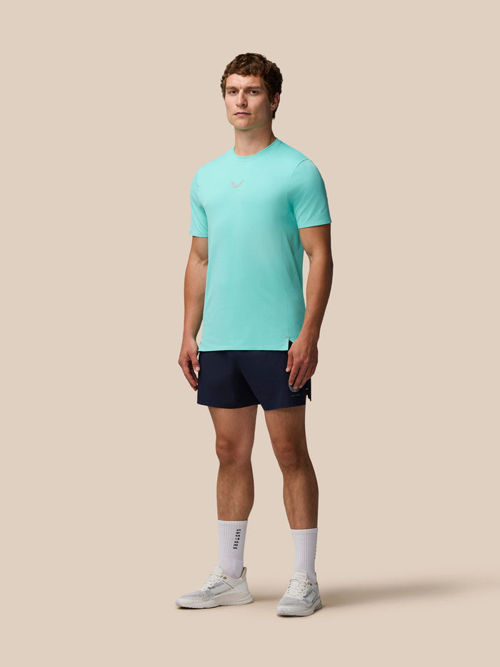 Full-body shot of a man wearing a light aqua Zone Training T-Shirt with navy shorts on a beige background