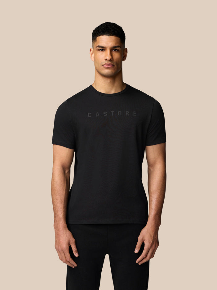 Male model in black Graphic Lifestyle T-Shirt with Castore graphic, full body shot on beige background.