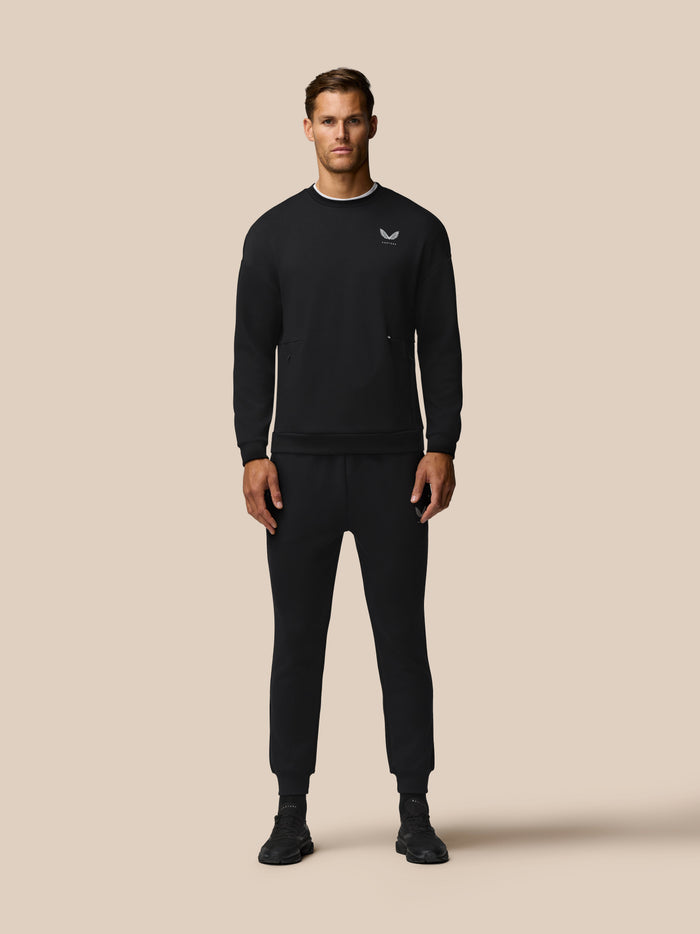 Model wearing a black Travel Lifestyle Sweatshirt with a small white crest logo on the chest.