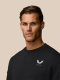 Head and shoulders view of a man in a black crew neck sweatshirt with a small white crest on the chest.