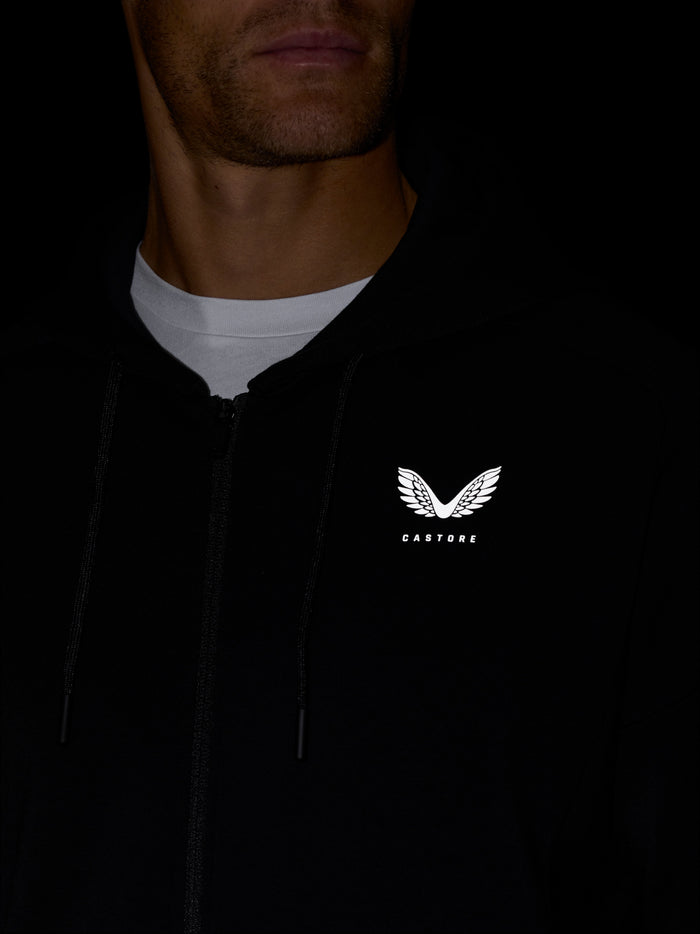 Close-up of black Travel Zip Hoodie worn by a model showing left chest Castore logo and zipper.