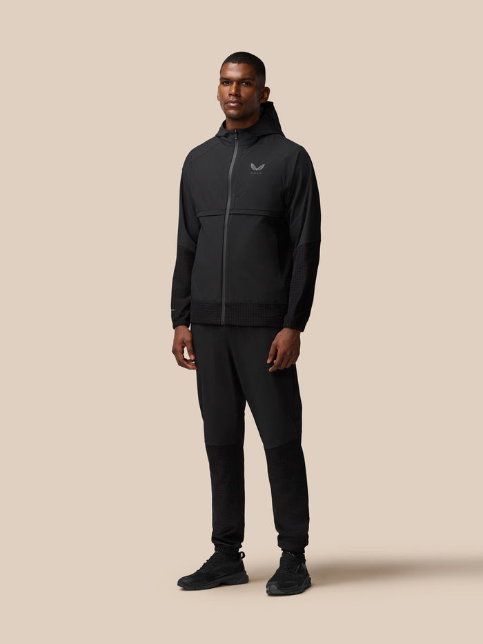 Male model wearing black Flex Winterised Woven Jacket with Castore logo on the chest, full-body shot.