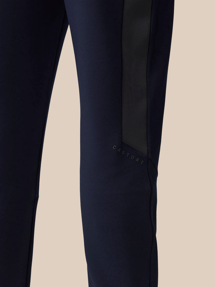 Close-up of navy pant leg showing a black stripe and Castore branding.