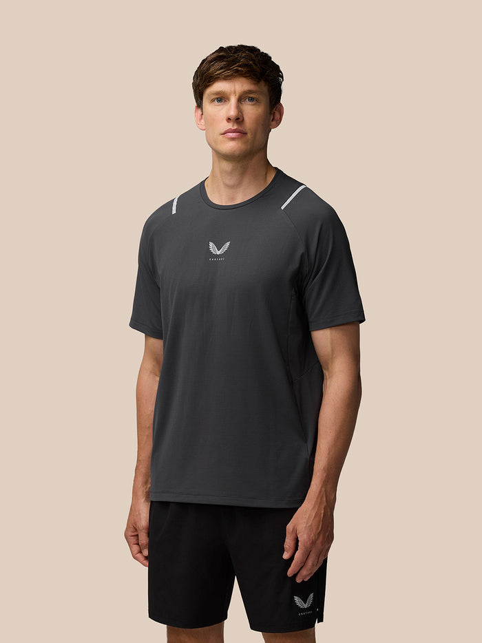 Three-quarter rear view of a man in gunmetal Apex Training T Shirt with reflective shoulder accents and Castore branding at the hem.