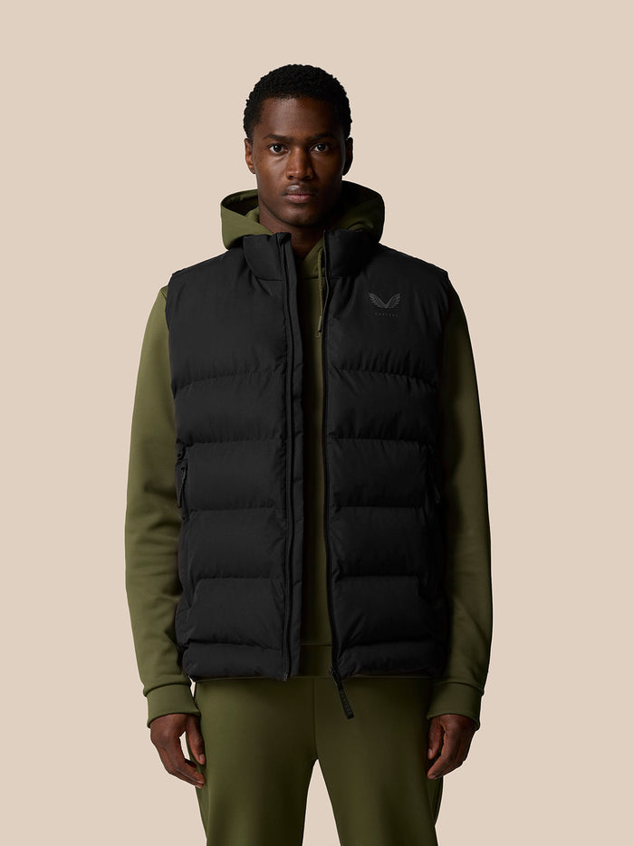 Man wearing a black sleeveless puffer vest over an olive hoodie with a front zipper