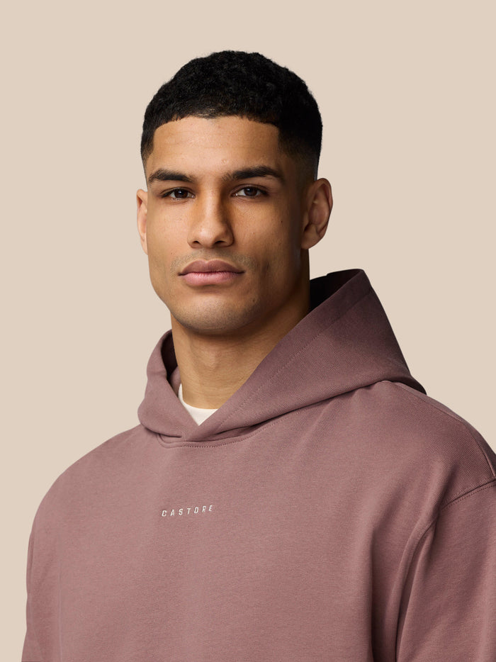 Portrait of a model wearing Adapt Lifestyle Hoodie in mauve with hood down and Castore logo on the chest.