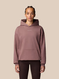 Full-body shot of male model wearing mauve Adapt Lifestyle Hoodie with hood down against beige backdrop