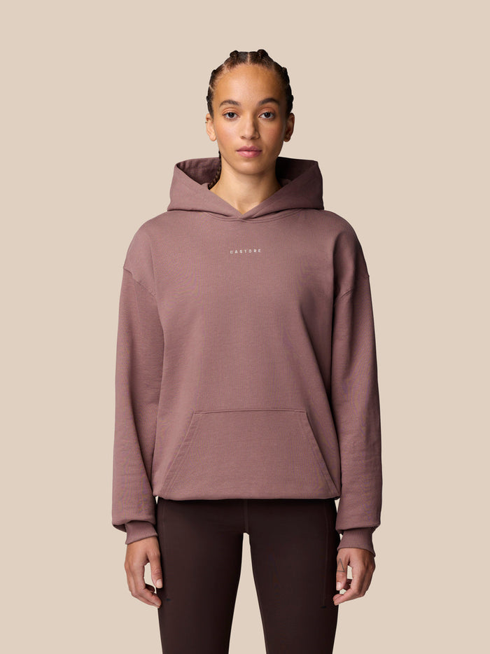 Full-body shot of male model wearing mauve Adapt Lifestyle Hoodie with hood down against beige backdrop