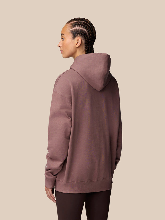 Back view of a model wearing Adapt Lifestyle Hoodie in mauve with braided hair and the hood resting at the back.