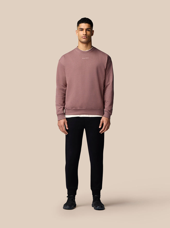Male model wearing mauve Adapt Lifestyle Sweatshirt with oversized fit, paired with black joggers and white sneakers.