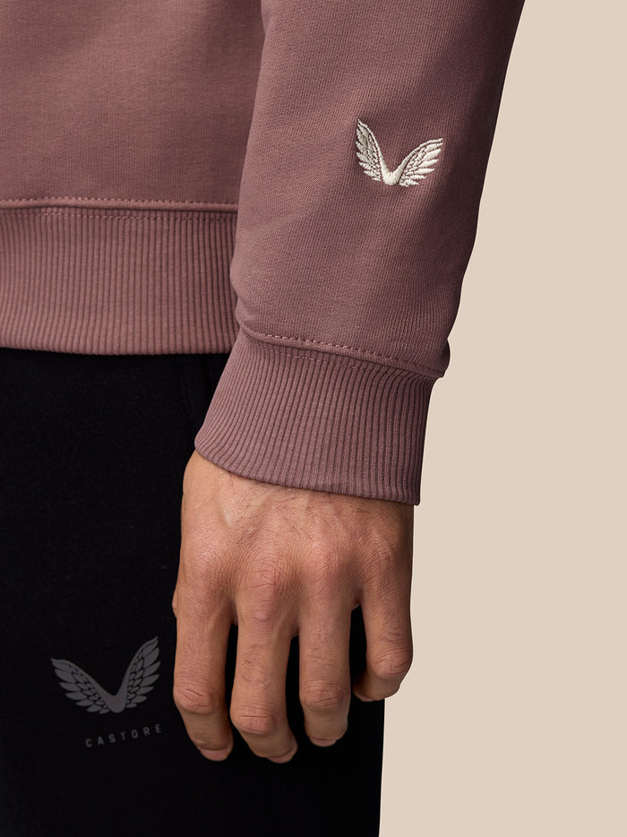 Close-up of mauve sweatshirt cuff showing white embroidered Castore wing logo on the sleeve