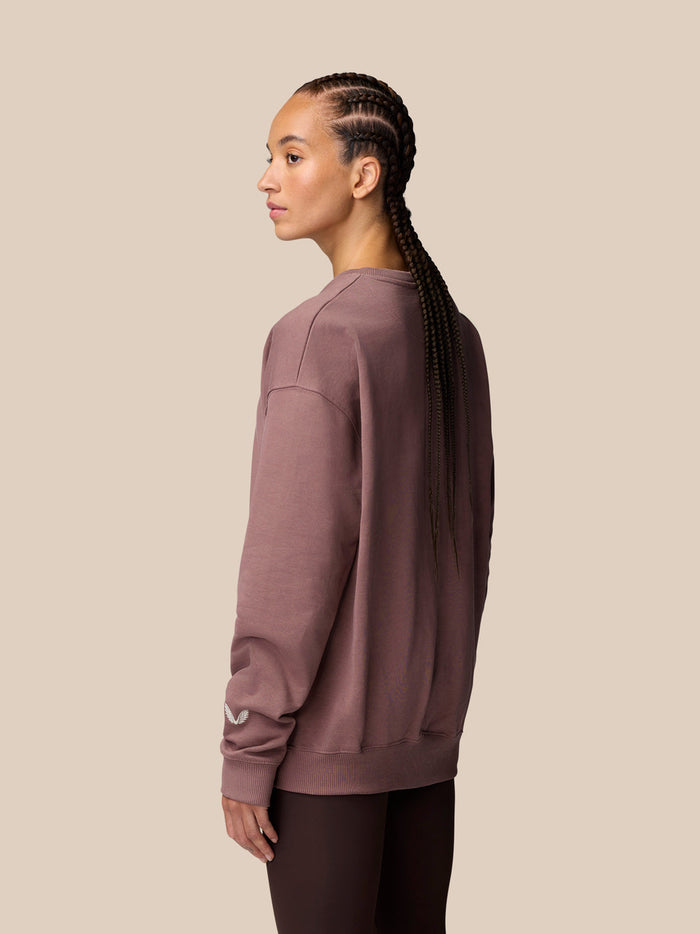 Side view of model in mauve Adapt Lifestyle Sweatshirt with oversized silhouette and Castore wing logo on left sleeve.